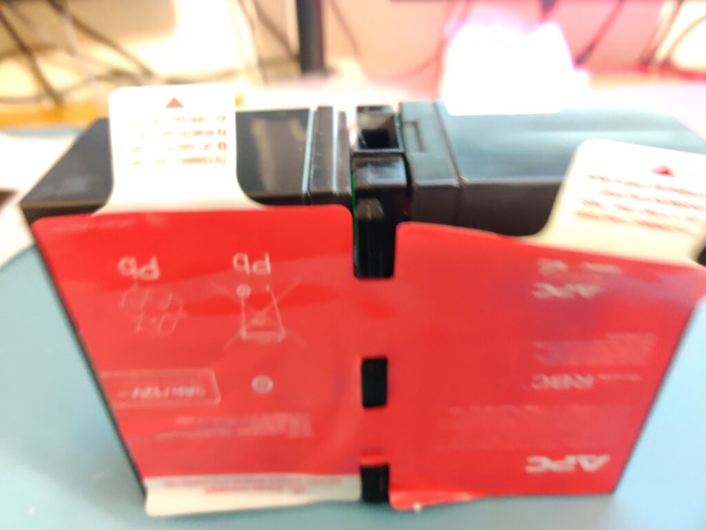 The sealed cartridge: a red APC sticker plate wrapped over two cells, pull tabs standing up at the top